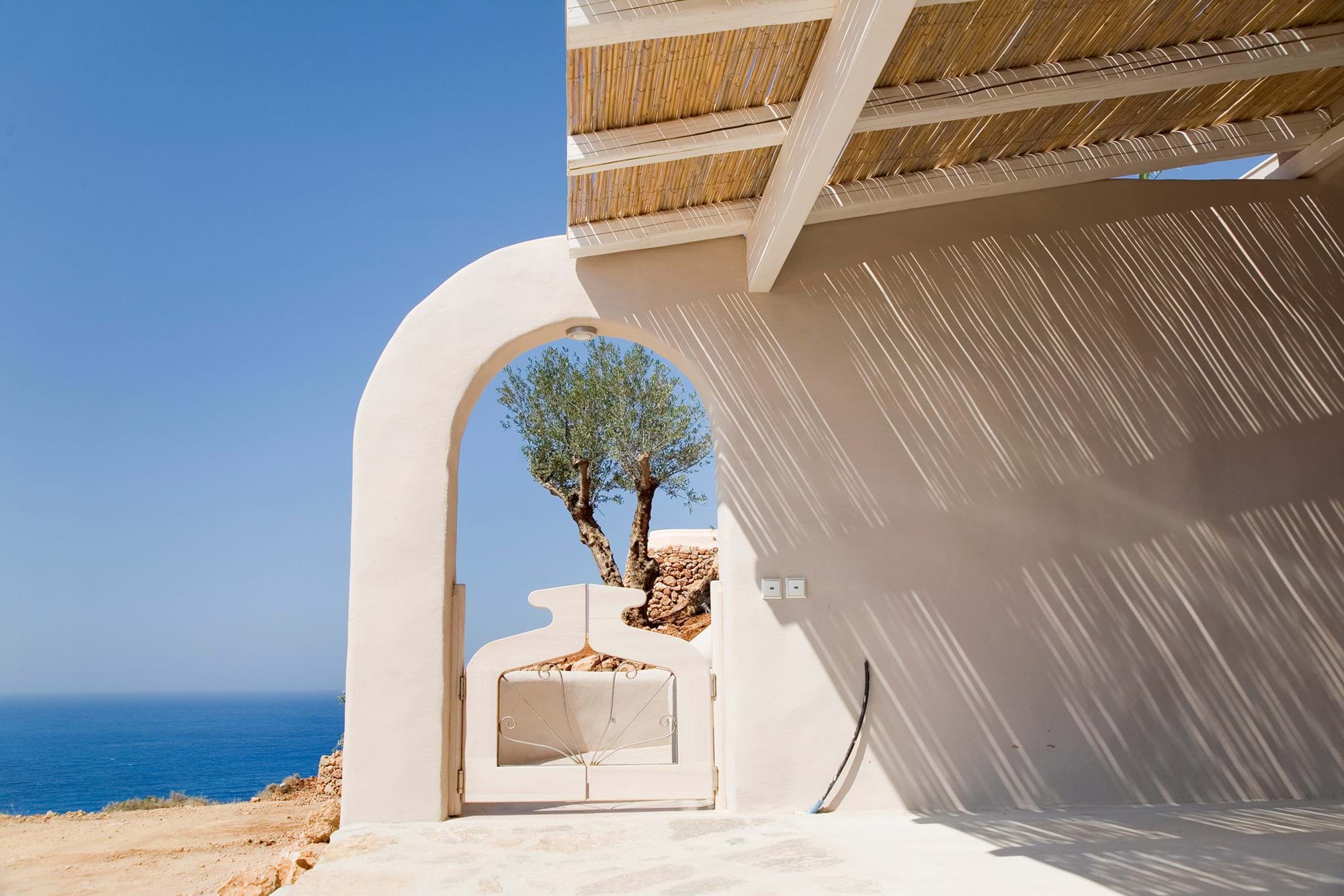 Whitewashed arch framing an olive tree and the sea